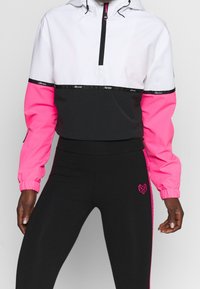 Färgblockerad jacka i vitt, svart och rosa med halvdragkedja; svarta leggings med ett rosa hjärtmönster och sidosträck.