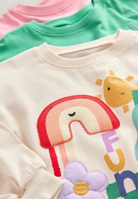 Három crewneck pulóver egymásra rakva: egy krémszínű, szivárvány grafikával, egy zöld és egy rózsaszín. Puha pamut anyag, színes mintákkal.
