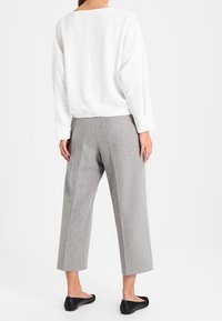White top with long sleeves, textured panel, and elastic hem; gray tailored wide-leg pants with a mid-calf length; black flat shoes.