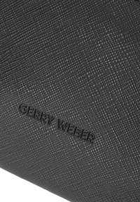 Materiale sintetico nero texture con una finitura decorata, caratterizzato da un marchio in rilievo "GERRY WEBER" sulla superficie.