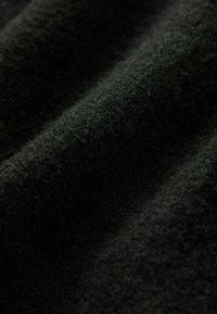 Sort uldstof med en blød, struktureret overflade, der har diskrete fibre og et let bølget udseende over folderne.
