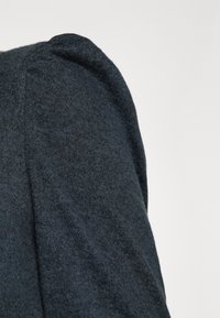 Mörkgrå stickad tröja, närbild av axeln med rundade detaljer och en mjuk textur.