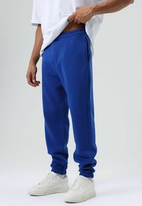 Blauwe joggingbroek met elastische boorden, steekzakken en een trekkoord in de taille, gecombineerd met witte sneakers en een los wit t-shirt.