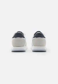 Zapatillas deportivas blancas con un upper liso, acentos de ante en el talón y un cuello de malla negra. Presenta una suela acolchada para mayor comodidad.