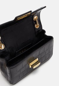Černá kabelka s embosovaným vzorem krokodýla, se zlatým uzávěrem a řetízkovými doplňky, obsahující podšitou vnitřní část se zipovou kapsou a logem.