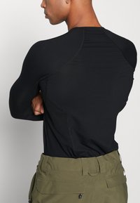 Camisa atlética negra de manga larga con diseño ajustado y mangas raglán, combinada con pantalones cargo verde oliva que presentan bolsillos de utilidad.