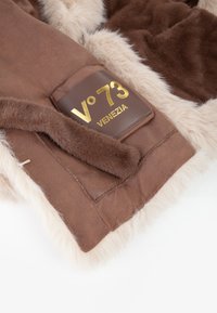 Giacca marrone foderata in pelliccia con morbido bordo in pelliccia sintetica beige, caratterizzata da un'etichetta in pelle marrone incisa con "V°73 VENEZIA" in oro.