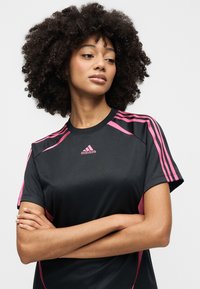 Μαύρο αθλητικό μπλουζάκι με ροζ λεπτομέρειες και τρεις ρίγες στα μανίκια, με στρογγυλή λαιμόκοψη και εφαρμοστή σχεδίαση. Κατασκευασμένο από αναπνέον ύφασμα.