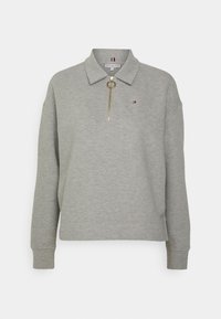 Pull à manches longues en ribbed gris clair avec col, demi-fermeture éclair à tirant doré, et petit logo rouge, blanc et bleu sur la poitrine.