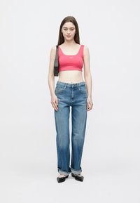 Top rosa cropped, jeans azuis de perna reta com bainhas dobradas e sapatos rasos pretos. Design simples, textura suave e ajuste casual.