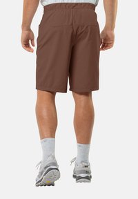 Shorts marron légers avec une taille élastique, des poches latérales et une texture lisse. Portés avec des chaussettes grises et des chaussures de plein air.