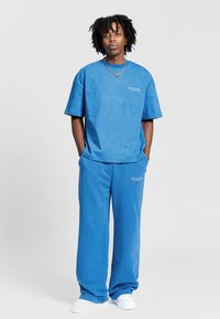 Blå bomulds oversized t-shirt og matchende vide bukser med tekstureret stof og subtilt logo-detalje. Hvide sneakers fuldender outfittet.