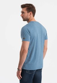 Camiseta de manga corta azul claro con un sutil patrón de puntos y un pequeño acento de marca en la manga. Tejido suave con un ajuste casual.