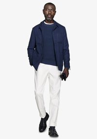 Marinejakke med to frontlommer over en ribbet marineblå sweater og hvide bukser; sorte sko og handsker fuldender outfittet.