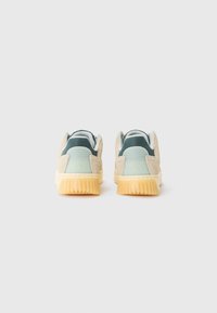 Baskets en suède beige et vert avec une texture douce. Forme arrondie, semelle striée de couleur gomme claire et détail de col rembourré.