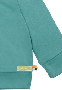 Felpa teal con maniche lunghe, dotata di polsini a coste e un'etichetta con "loud + proud" in accenti verdi e arancioni vicino all'orlo.