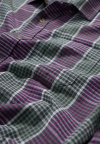 Camisa a cuadros con rayas horizontales y verticales en púrpura, verde y blanco, con una textura de tela suave y detalles de botones.