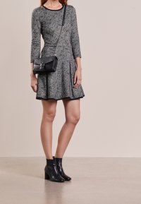 Robe à motifs gris et noirs avec manches trois-quarts, jupe évasée, accompagnée d'un sac bandoulière noir et de bottines noires.