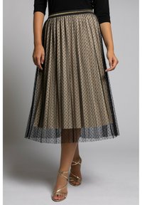 Jupe beige à pois avec un voile noir transparent, design plissé, ceinture dorée, et associée à des talons dorés à lanières.