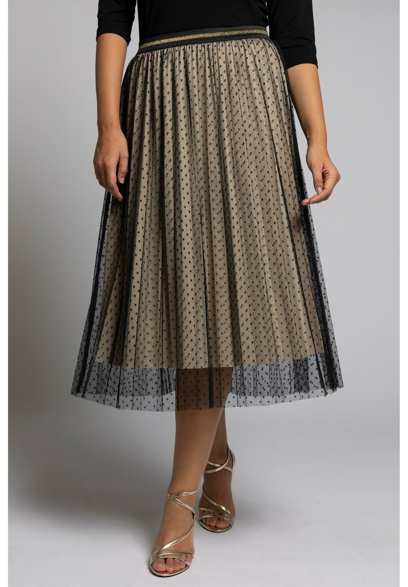 Jupe beige à pois avec un voile noir transparent, design plissé, ceinture dorée, et associée à des talons dorés à lanières.