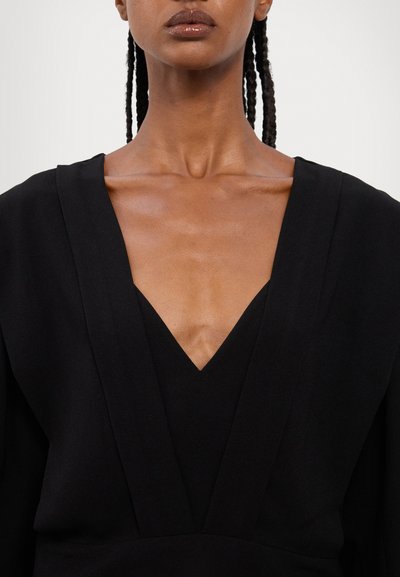 Black v-neck garment with structured shoulders. Smooth texture with a deep neckline and wide sleeves. Minimalistic design.