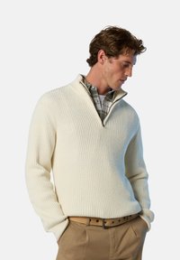 Maglione a coste crema con colletto a mezza zip, indossato sopra una camicia a quadri verde. Presenta maniche lunghe e una vestibilità rilassata.