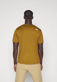 T-shirt de manga curta, na cor mostarda, feita de tecido suave, com um logo branco na parte superior das costas e um decote redondo clássico.
