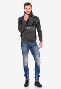 Grauem Pullover mit hohem Kragen, der mit dem auffälligen Aufdruck "RELAX" versehen ist. Kombiniert mit blauen Slim-Fit-Jeans und schwarzen Sneakers. Sanfte Textur, lässiger Stil.