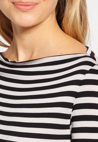 Czarny i biały top w paski z szerokim dekoltem, dopasowany krój, miękki materiał i gładka tkanina. Posiada poziome paski na całej powierzchni.