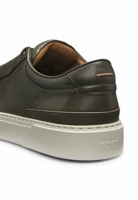 Mörkgrön lädersneaker med slät textur, vit gummisula och subtila sömnadsdetaljer. Har en bronsaccent på hälen.