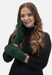 Groen gebreide wanten met geribde manchetten en een textuurafwerking. Bevat een klein bruin label op één van de wanten. Model poseert terwijl hij de wanten draagt.