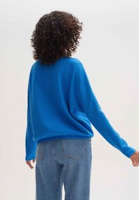 Niebieski, fakturowany, oversize'owy sweter z długimi rękawami, z ribbowanym wykończeniem. W połączeniu z jasnoniebieskimi dżinsami o wysokim stanie.