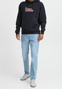 Sudadera con capucha azul marino con gráfico de "inc.", jeans rectos de mezclilla azul claro y zapatillas deportivas grises, con cordones y detalles en piel.