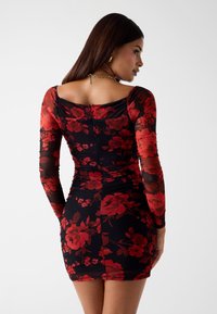 Bloemige jurk met rode rozen op een zwarte achtergrond. Lange doorschijnende mouwen, aansluitend ontwerp en gerimpelde textuur. Achterste ritsluiting.