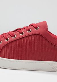 Baskets rouges avec une surface en mesh texturé, œillets en métal et lacets assortis. Semelle en caoutchouc blanche avec un motif décoratif.