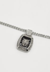 Collier en chaîne argentée avec un pendentif en forme de tête de lion, fond en quadrillage noir, bordé de cristaux transparents et d'accents texturés.