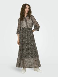 Abito maxi nero con motivo floreale realizzato in tessuto leggero e trasparente; presenta una parte superiore con colletto e bottoni e una vita cinchata, abbinato a sneaker bianche.