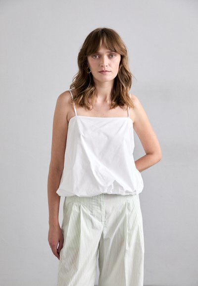 White, loose-fitting camisole with thin straps, tucked into light green, striped wide-leg trousers. Smooth fabric with minimal design.