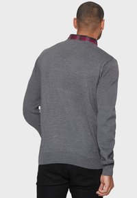 Maglione grigio lavorato a maglia con una trama a coste, collo rotondo e colletto a scacchi a contrasto. La vista posteriore mostra maniche aderenti e orlo dritto.