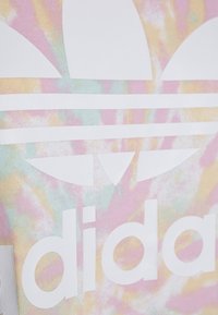 Flerfärgad tie-dye-tyg med en framträdande vit Adidas-logo och tre ränder, som visar en slät textur och mjukt utseende.