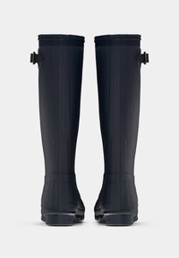 Bottes en caoutchouc noires, montantes jusqu'au genou, avec une finition lisse, une sangle réglable près du haut et une semelle robuste pour l'adhérence.