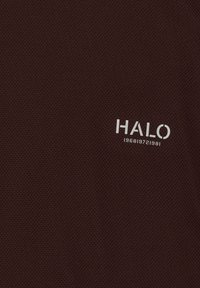 Dunkelbrauner Stoff mit kleinen Perforationen zeigt weißen Text „HALO“ und eine Zahlenfolge darunter: 1968 1972 1981.