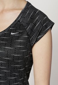 Svart skjorta med vita prickar, med rund halsringning och korta ärmar. Nike-logotyp i silver på vänster bröst.