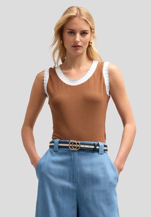 Top marrone senza maniche con scollatura arricciata bianca e azzurro chiaro; abbinato a pantaloni blu a vita alta e una cintura a righe con una fibbia dorata.