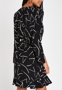 Svart klänning med vita abstrakta mönster, långa ärmar, nyckelhålsrygg, indragen midja och volangkant nederst.