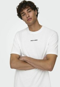 T-shirt bianco in cotone con colletto a girocollo e maniche corte. Presenta la scritta ricamata nera "ONLY & SONS" sul petto.