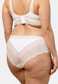 Ensemble de lingerie blanche avec un dos en dentelle à bords festonnés. Le soutien-gorge dispose de bretelles réglables et d'une fermeture à agrafes. Devant en tissu lisse.