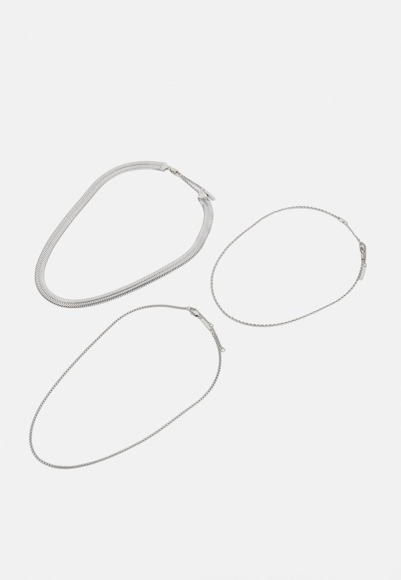 Tre collane d'argento: una collana a maglia a serpente spessa, una collana fine e una collana leggermente strutturata, tutte con chiusure e finiture lisce.