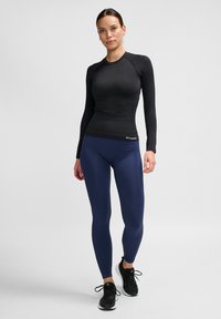 Langärmliges schwarzes Sportoberteil kombiniert mit marineblauen Leggings. Das Oberteil hat ein figurbetontes Design, während die Leggings glatt mit einem leichten Schimmer sind.