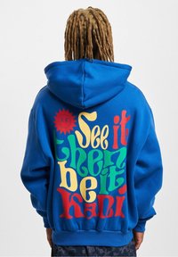 Sudadera azul con capucha con un gran gráfico de texto multicolor en la espalda. Cuenta con un ajuste relajado y puños y dobladillo acanalados.